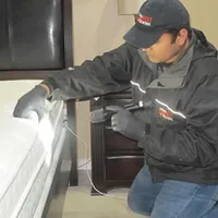 Bed bug inspection technician checking a mattress and bed frame for signs of infestation in Grand Rapids, MI