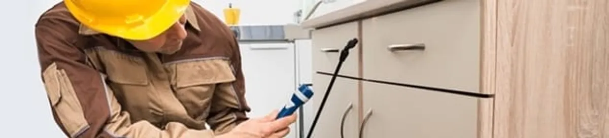 Roach exterminator applying treatment under kitchen cabinets in Grand Rapids, MI