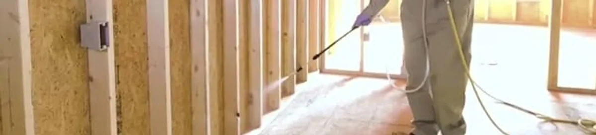 Termite treatment technician applying spray along framing and unfinished walls in Grand Rapids, MI